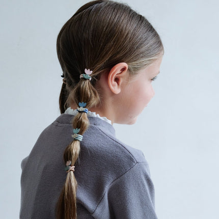 Person with a ponytail decorated with colorful hair ties on a light gray background