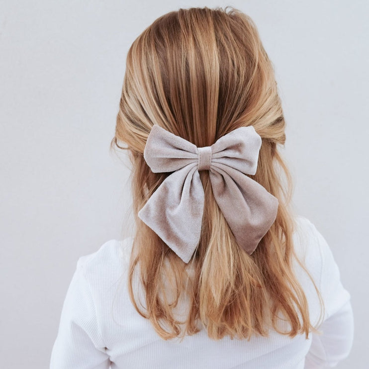 Blonde hair with a large beige bow on a plain background