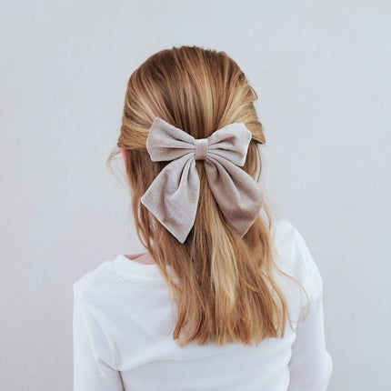 Person with a large beige bow in their hair against a plain background