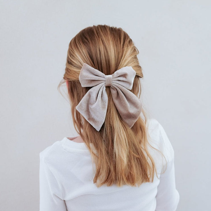 Person with a large beige bow in their hair against a plain background