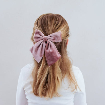 Person with pink hair bow in a half-up hairstyle against a light gray background