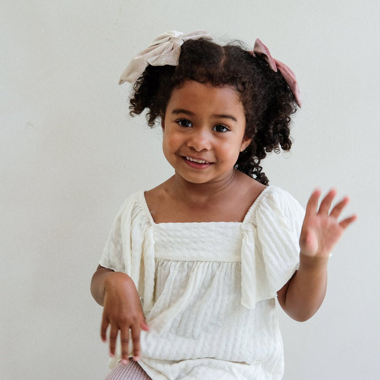 Young girl in a white top with floral hair accessories on a plain background