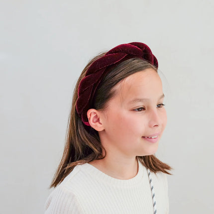 Young girl wearing a burgundy velvet headband on a light gray background