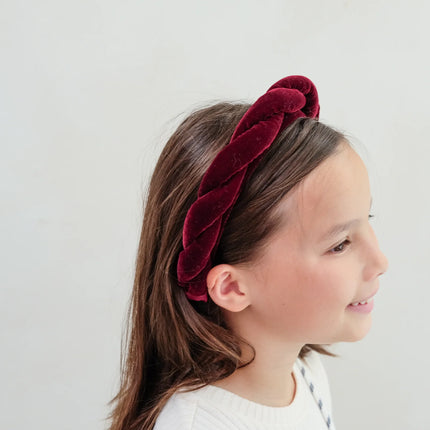 Young girl wearing a red velvet headband against a white background
