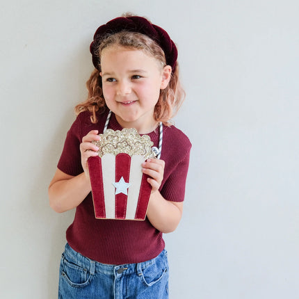 Young girl holding a decorative popcorn box with a star on a plain background