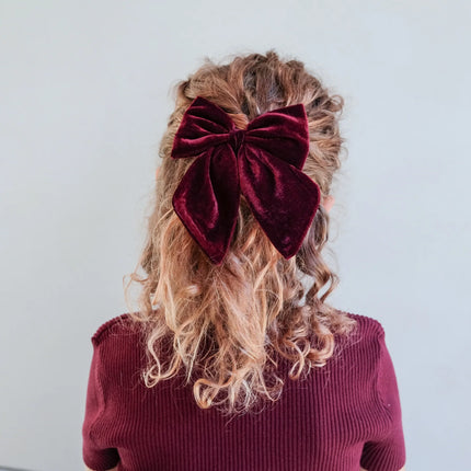 Person with curly hair wearing a large burgundy bow and a matching top against a white background