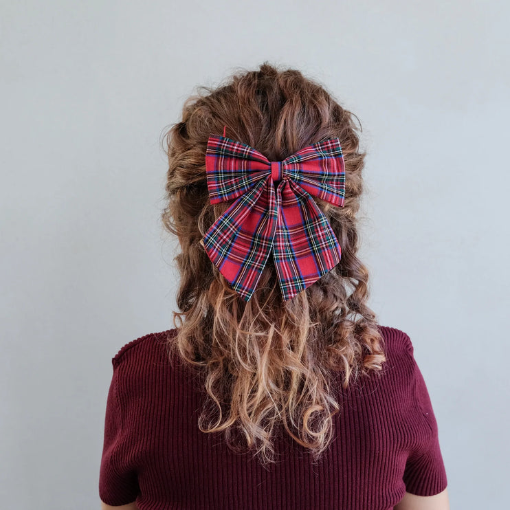 Person with plaid bow in curly hair against a plain background