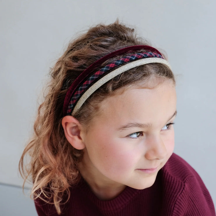 Young girl wearing a plaid headband against a plain background