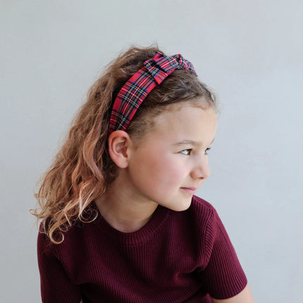 Young girl wearing a red plaid headband against a plain background