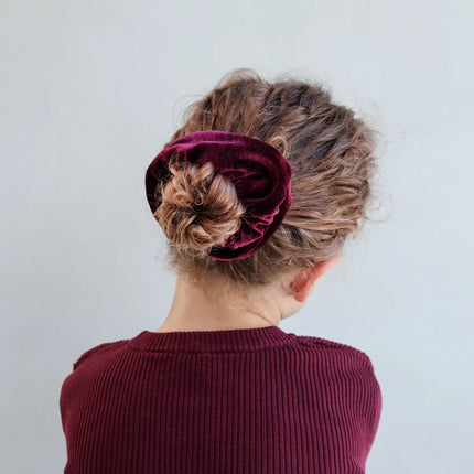Person wearing a burgundy scrunchie in their hair against a plain background