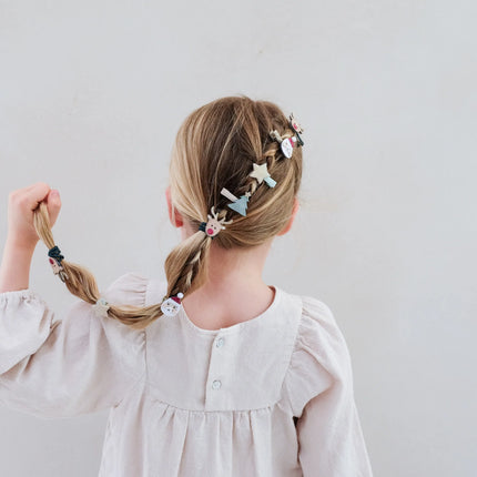 Child with braided hair adorned with decorative hair clips against a plain background
