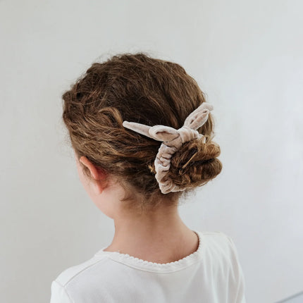 Person with braided hair wearing a scrunchie on a plain background