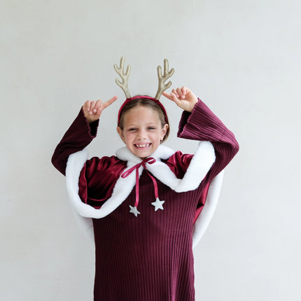 Child wearing a festive outfit with antlers and a white background