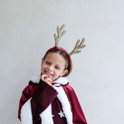Child wearing a red cape and reindeer antlers on a plain background