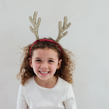 Child wearing gold glittery reindeer antlers on a plain background