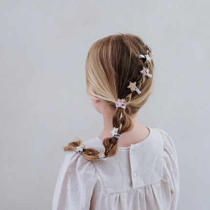 Child with braided hair adorned with star-shaped hair clips on a plain background