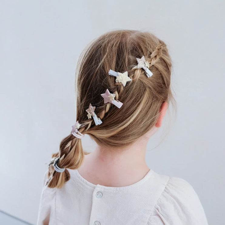 Child with braided hair wearing star-shaped hair clips on a plain background