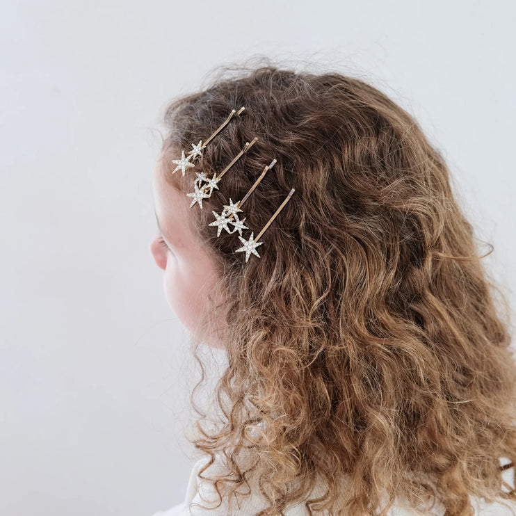Person with curly hair wearing gold star-shaped hair accessories on a white background