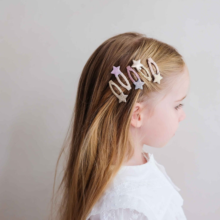 A kid wearing three metallic star-shaped hair clips in silver, gold, and rose gold