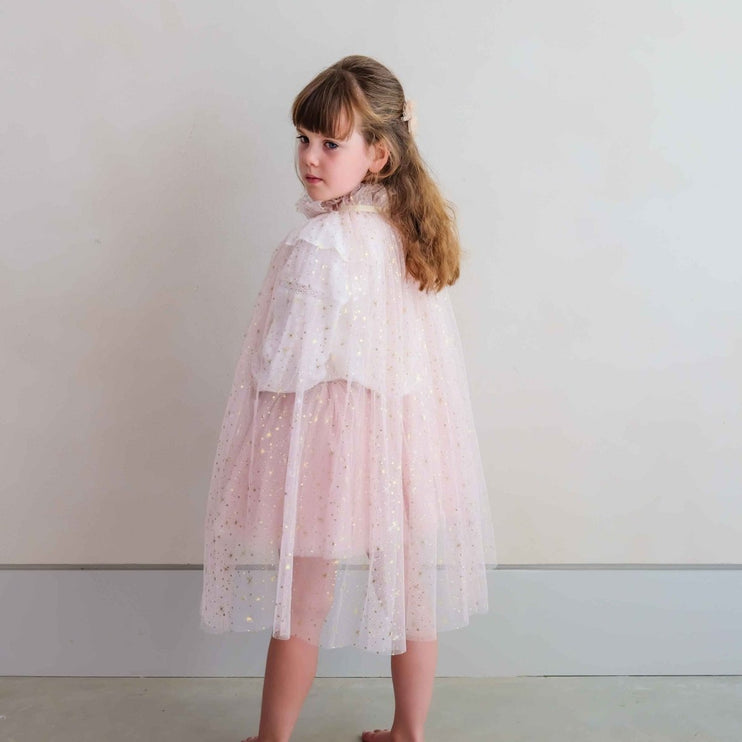 A young girl wearing a light pink and white sparkly tulle cape dress