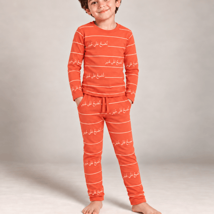 A young boy wearing a matching orange and white striped pajama set with white Arabic script