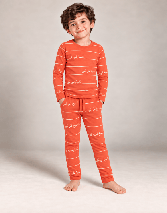 A young boy wearing a matching orange and white striped pajama set with white Arabic script