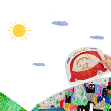 A hand holds a white paper craft or card featuring a red car illustration with Arabic text, shown against a white background with a yellow sun, blue clouds, and a colorful painted landscape at the bottom.
