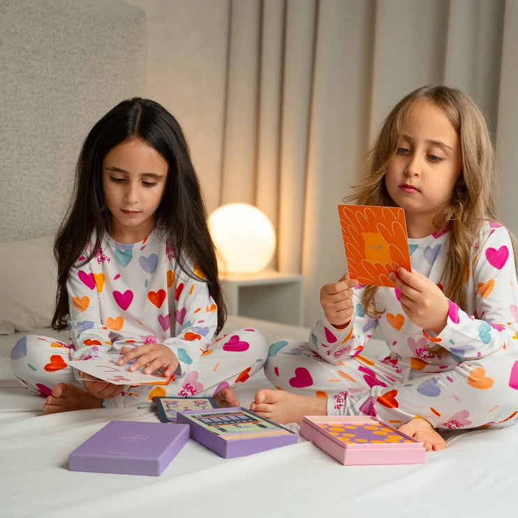 Two children in Albi  pajamas playing with colorful card games on a bed.