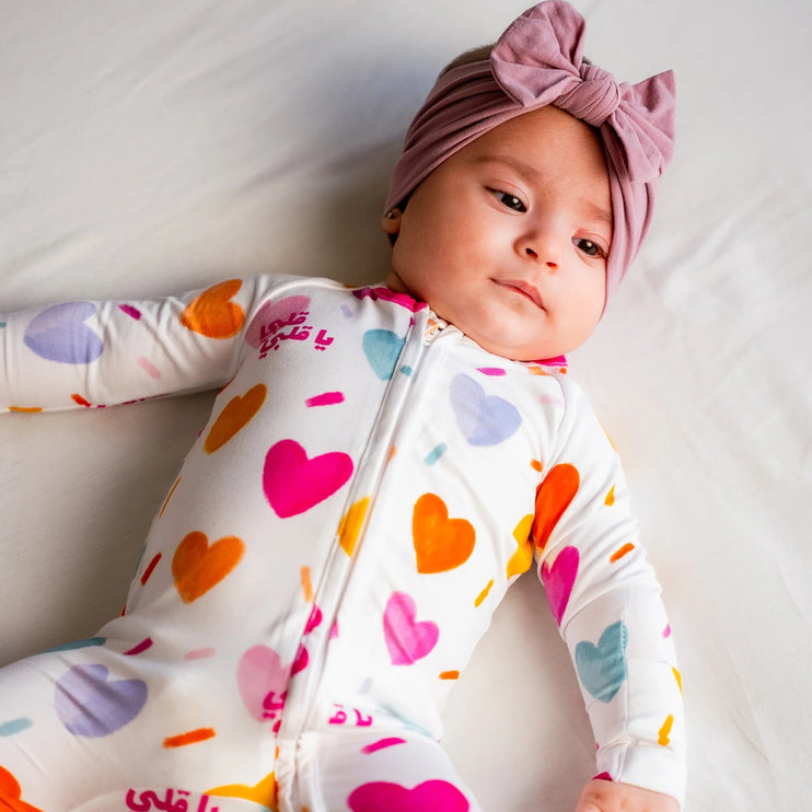 Baby wearing a colorful heart-patterned onesie and pink headband on a white background