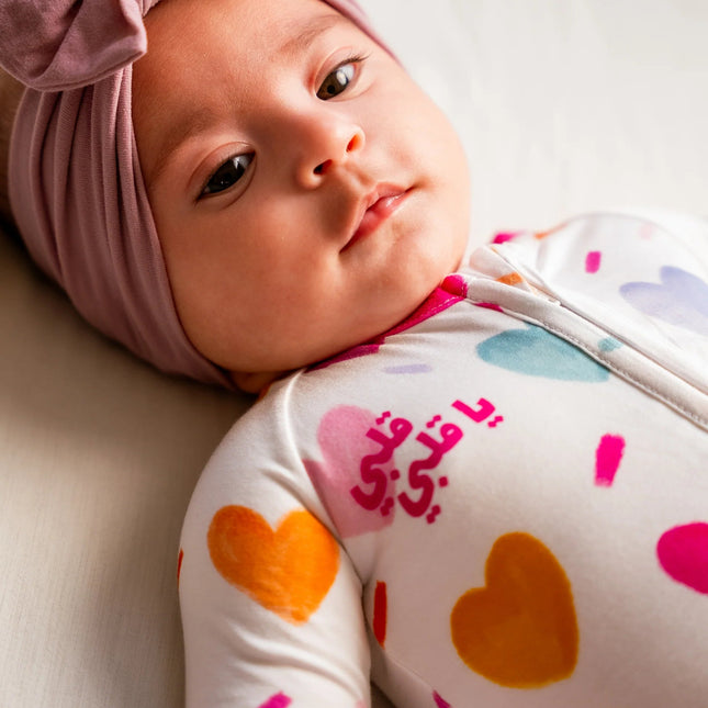 Baby wearing a pink headband and a onesie with colorful heart patterns on a light background