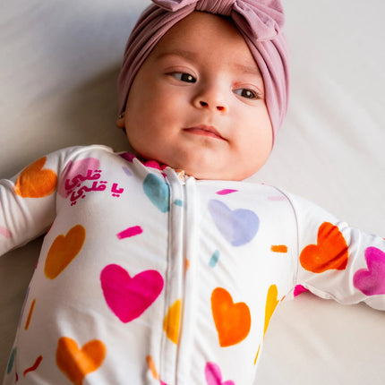 Baby wearing a colorful heart-patterned onesie and a pink headband.