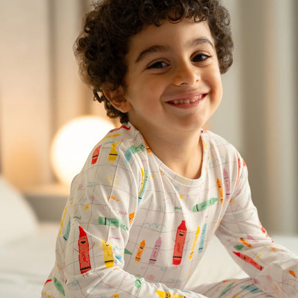 A child wearing Alwan pajama colorful crayon illustrations and text sitting on the bed.