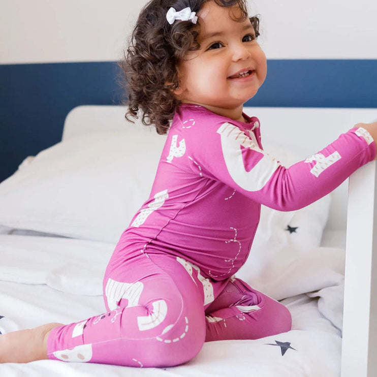 Child wearing Arqam onesie with white patterns on a bed