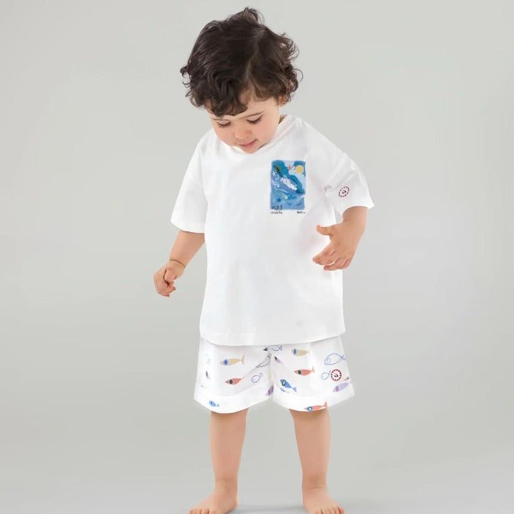 Child wearing a white t-shirt with a colorful design and shorts with 