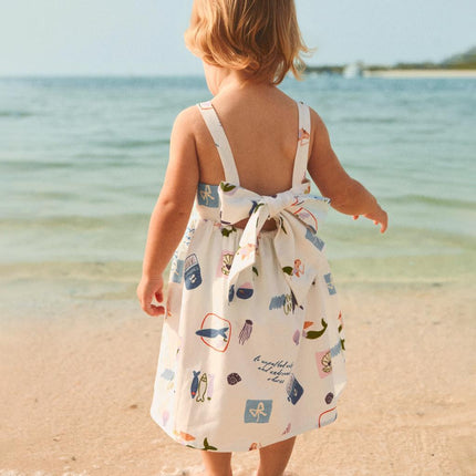 Child in a patterned dress standing on a beach 