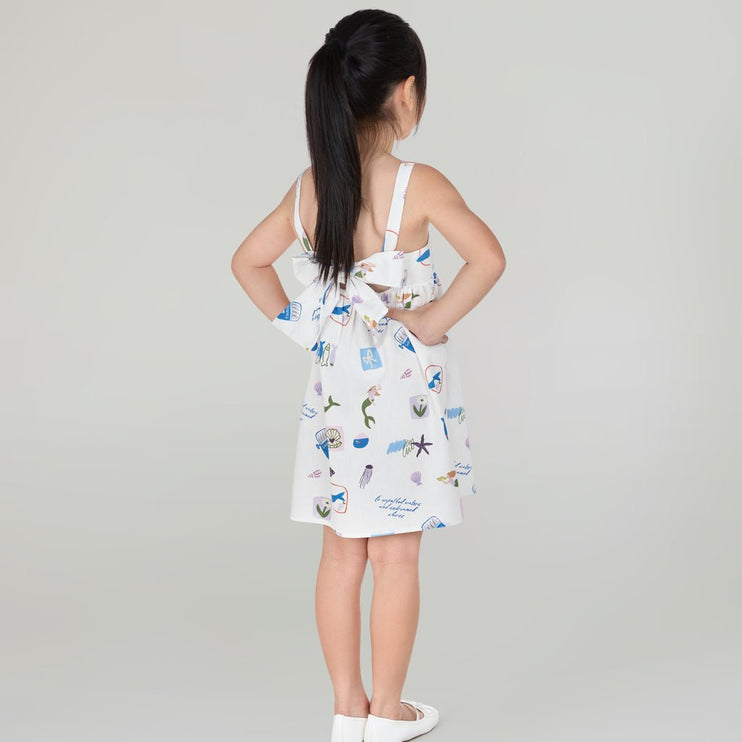 Young girl wearing a white dress with colorful patterns and a bow detail on the back
