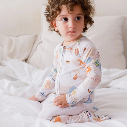 Child wearing a patterned onesie sitting on a bed with white bedding.