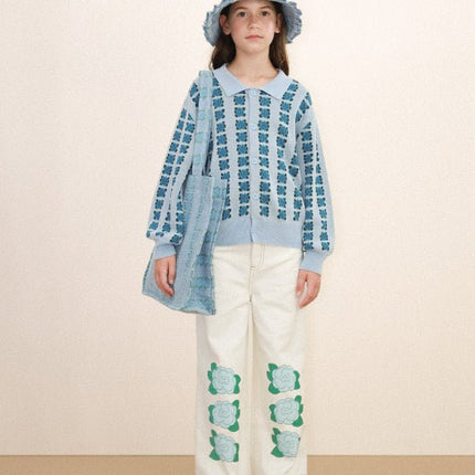 Baby wearing a blue patterned sweater and white pants with green designs