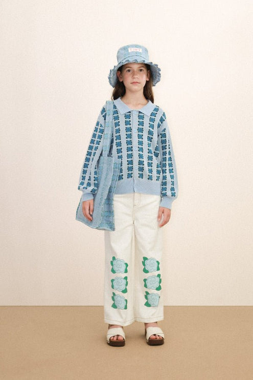 Baby wearing a blue patterned sweater and white pants with green designs