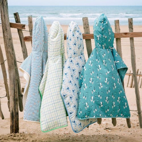 Colorful Boys Swim Ponchos hanging on a wooden fence featuring various pattern prints 