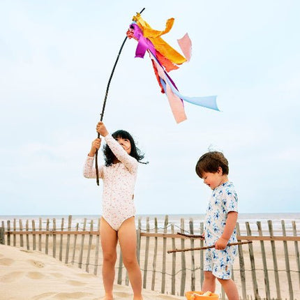 Boy in cream swimwear with blue monkey prints and girl in peach long-sleeve swimwear with butterflies print playing on the beach.
