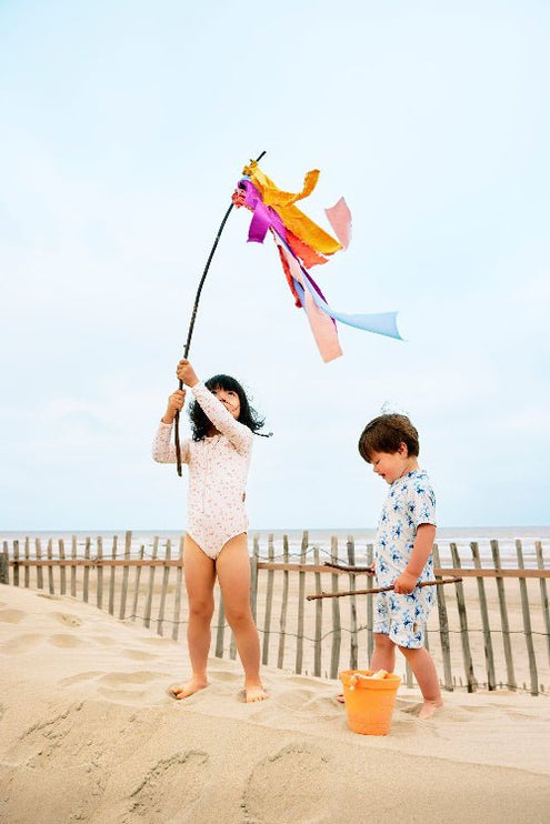Boy in cream swimwear with blue monkey prints and girl in peach long-sleeve swimwear with butterflies print playing on the beach.
