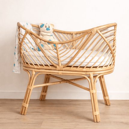 Wooden crib with a white mattress and a teddy bear inside, against a plain wall.