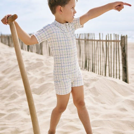 Playful baby boy wearing a cream swimsuit with blue and green stripes