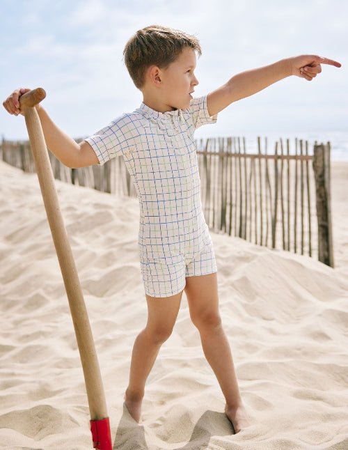 Playful baby boy wearing a cream swimsuit with blue and green stripes