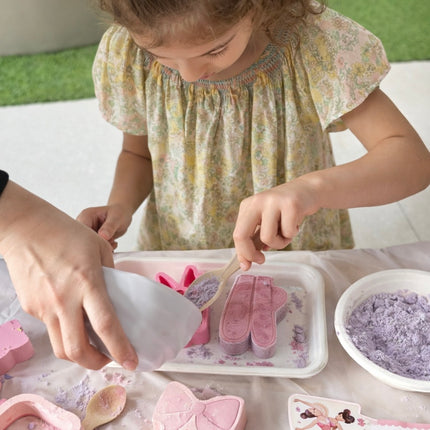 Child playing with pink and purple bathbomb mixture at a table.
