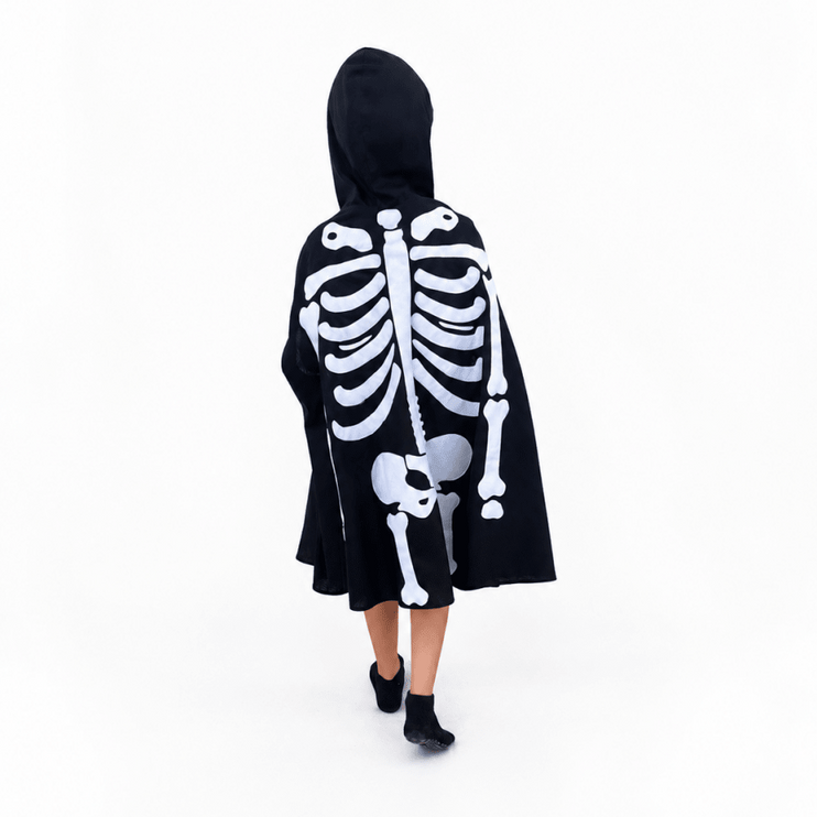 A child viewed from behind wearing a black hooded cape with a large white skeleton print, standing against a plain white studio background.