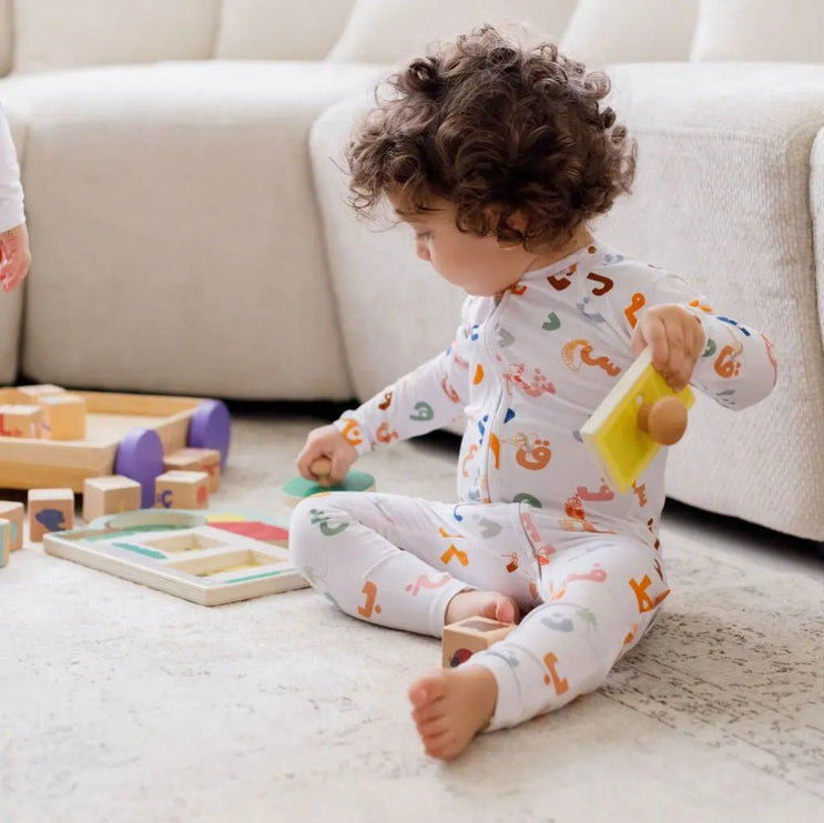 Child wearing Huroof onesie playing with toys on a carpeted floor