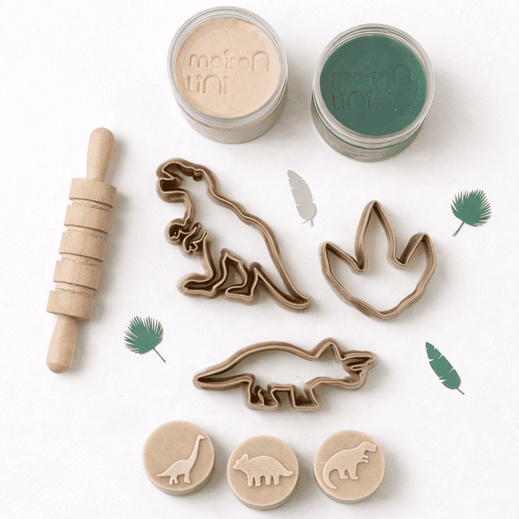 Cookie cutters with dinosaur designs and two jars of playdough on a white background.