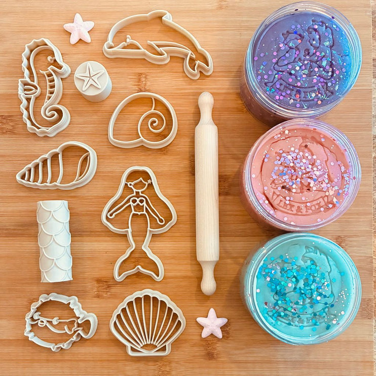 An undersea-themed cutters set featuring three jars of glittery playdough in purple, pink, and blue, and a wooden rolling pin.
